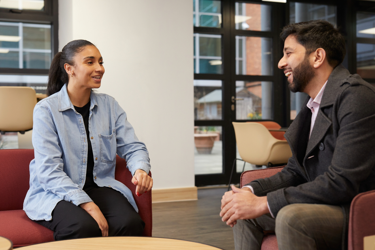 Two mixed heritage social workers sit talking in a Local Authority break out room.
