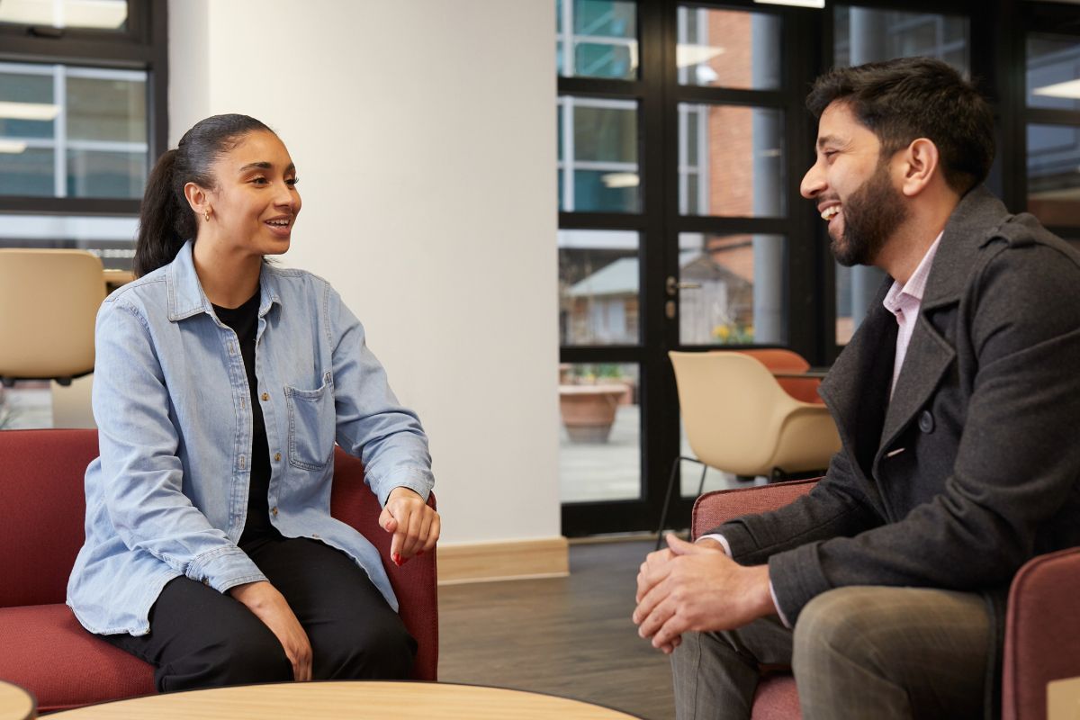 Two mixed heritage social workers sit talking in a Local Authority break out room.
